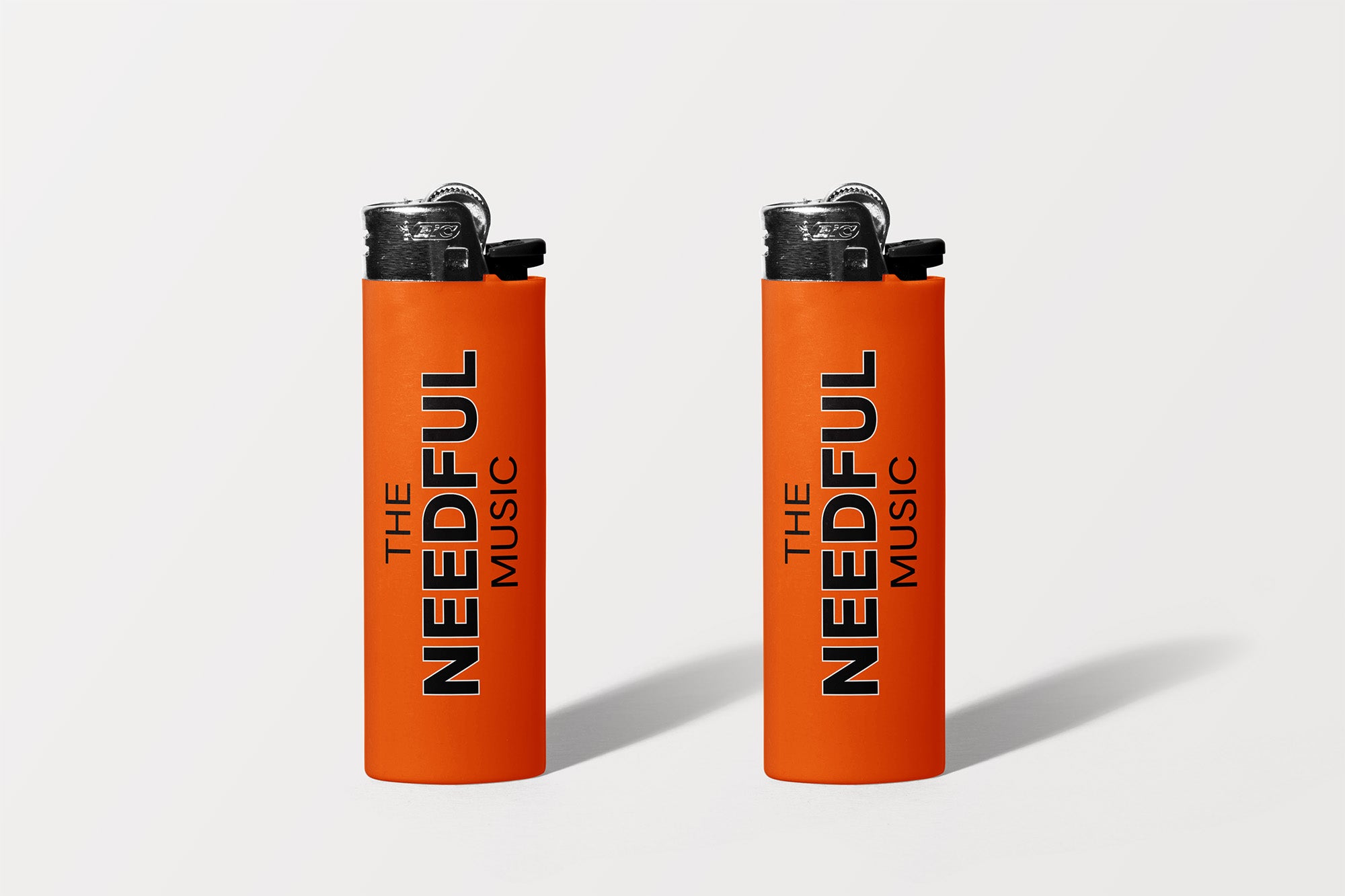 Two orange lighters with 'The Needful Music' branding on a white background