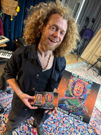 Glenn holding 'The Needful Rising Angels' album and merchandise in a studio setting