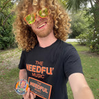 Vocalist Glenn wearing a black 'The Needful Music' t-shirt outdoors with greenery in the background