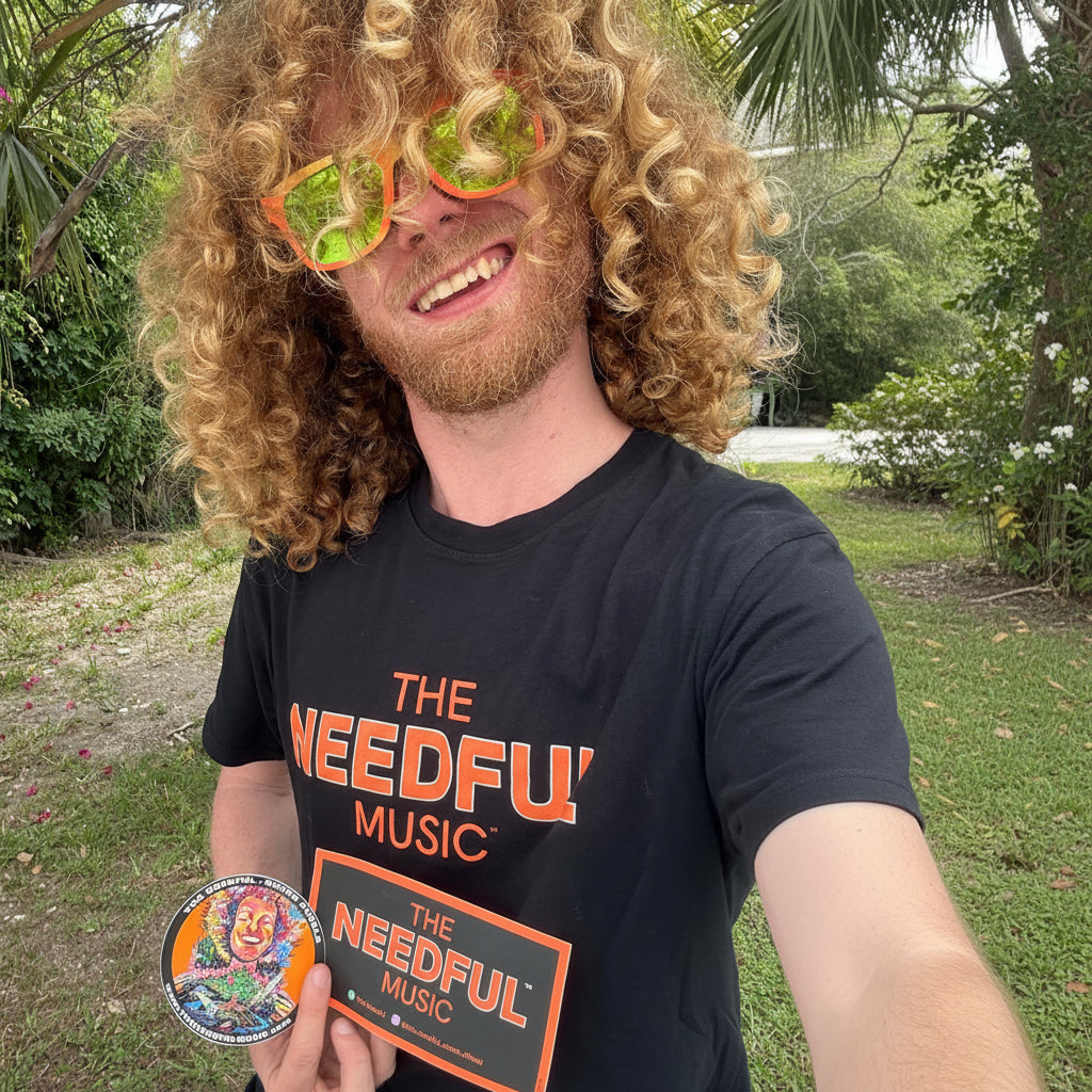 Vocalist Glenn wearing a black 'The Needful Music' t-shirt outdoors with greenery in the background