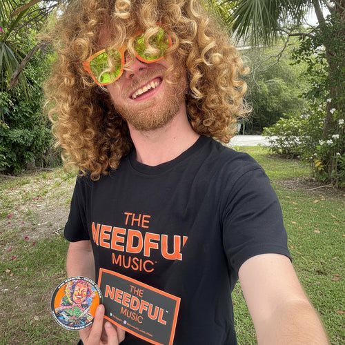 Vocalist Glenn wearing a black 'The Needful Music' t-shirt outdoors with greenery in the background