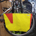 Yellow recycled tote bag with red accents attached to a bicycle wheel