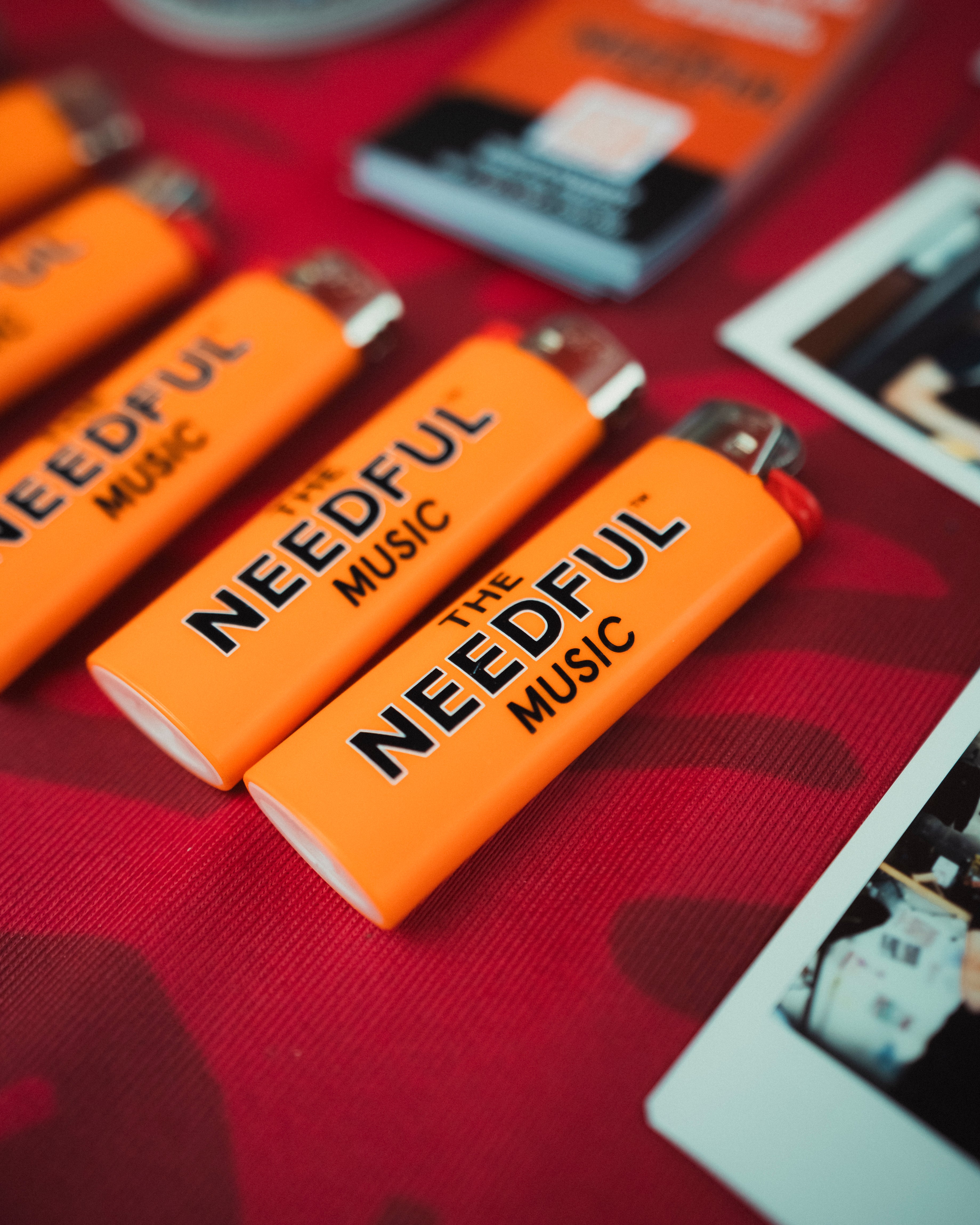 Orange lighters with 'The Needful Music' branding on a red surface.