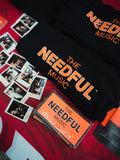 Black t-shirt with 'The Needful Music' branding on a red background with stickers and polaroid pictures of the band.