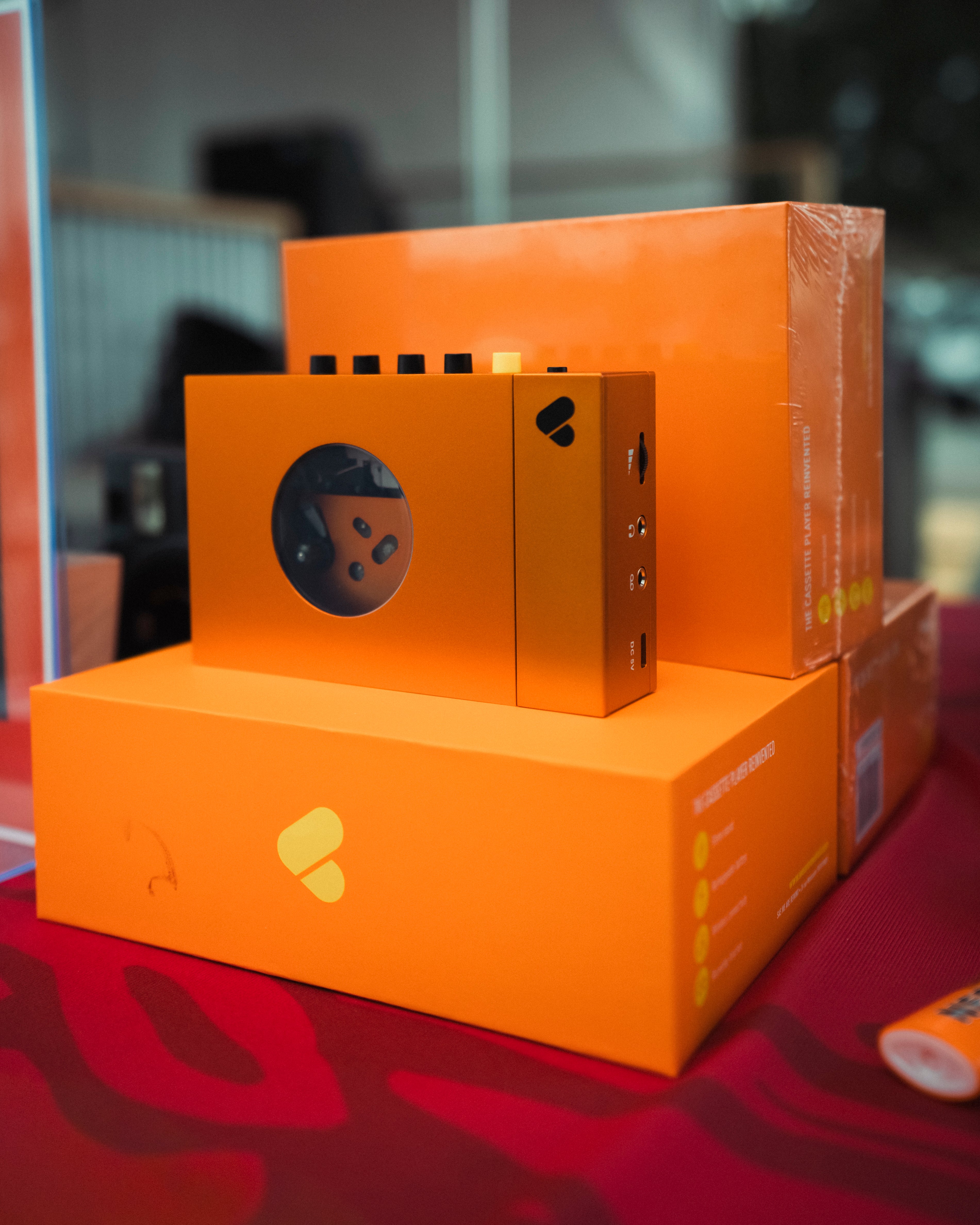 An orange We Are Rewind walkmans in original boxes, on a red surface